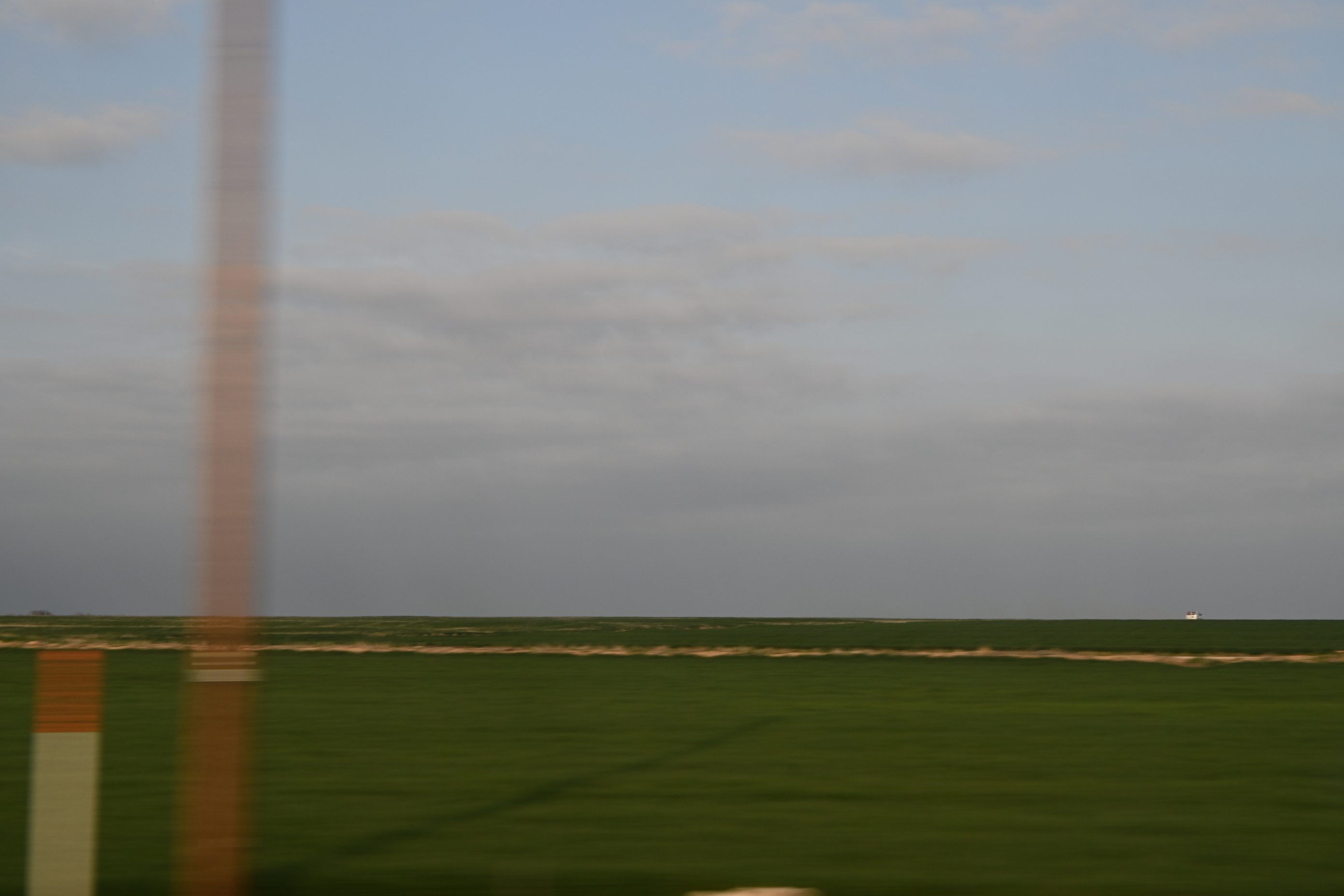 color photo of a green field composing a flat horizon, with blurred pylons in the foreground